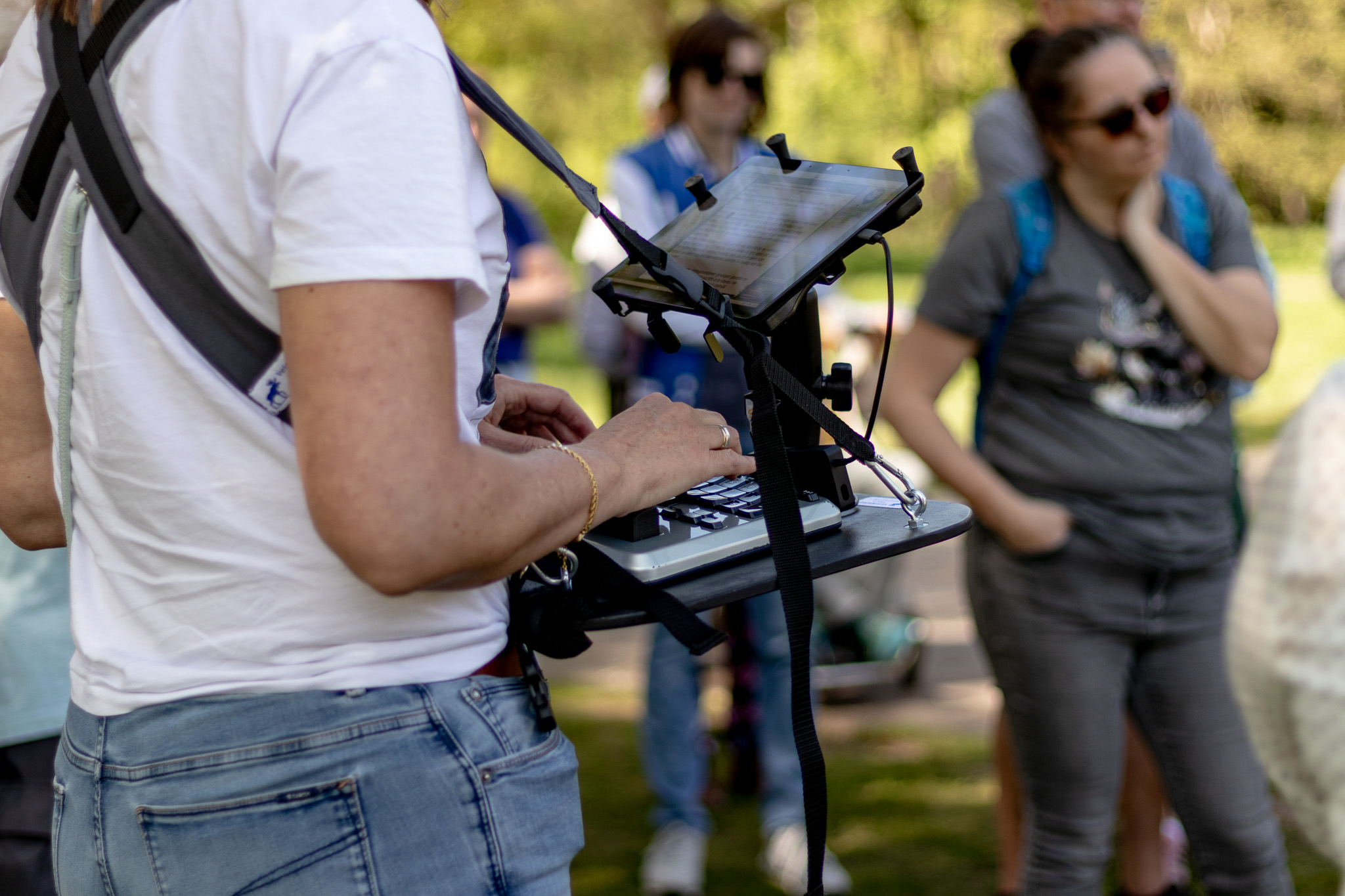 Persoon met een draagbare toetsenbord- en tabletopstelling, staand buiten in een groep mensen